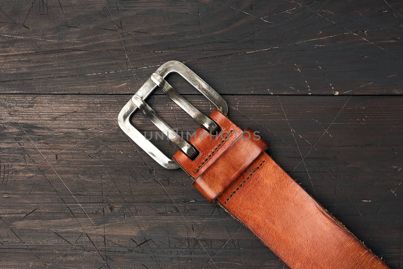 brown leather men's belt with metal buckle on a wooden backgroun by ndanko