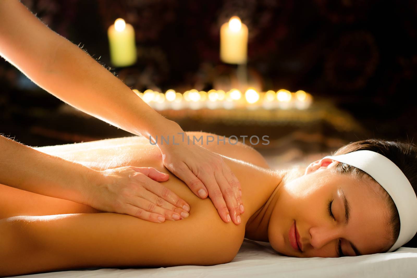 Close up of therapist massaging female spine in spa. Low key atmosphere with out of focus candles glowing in background.