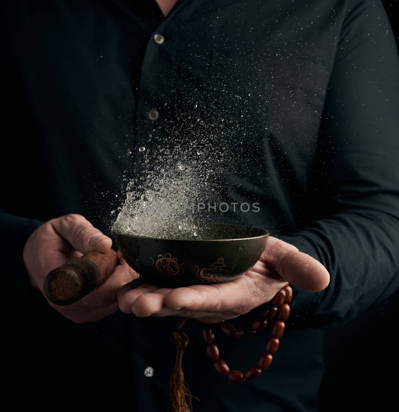 adult man in a black shirt rotates a wooden stick around a copper Tibetan bowl. ritual of meditation, prayers and immersion in a trance. Alternative treatment