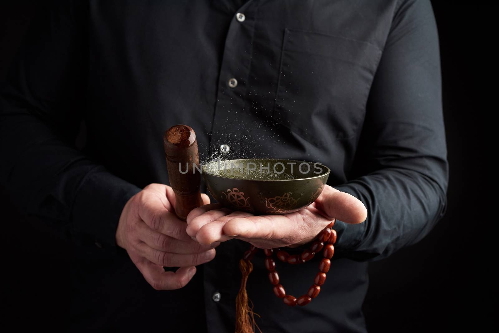 adult man in a black shirt rotates a wooden stick around a copper Tibetan bowl of water. ritual of meditation, prayers and immersion in a trance. Alternative treatment