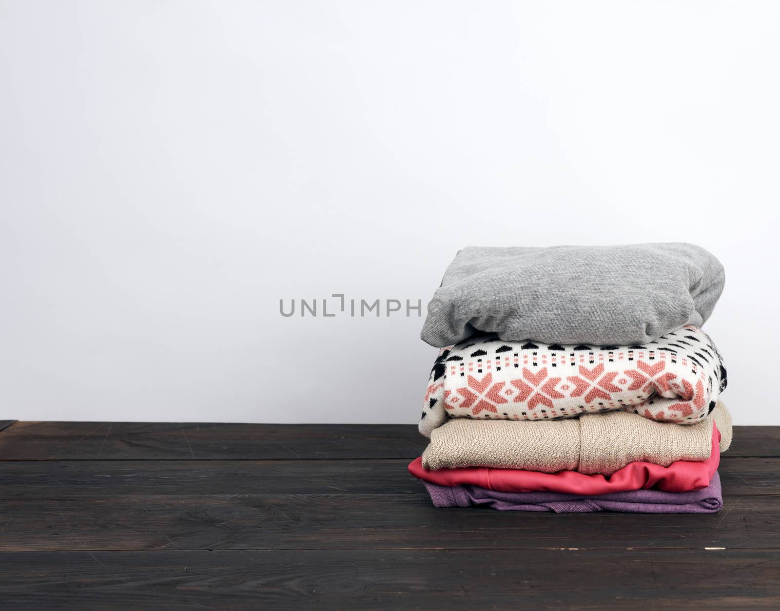 stack of various folded clothes on a wooden table, white backgro by ndanko