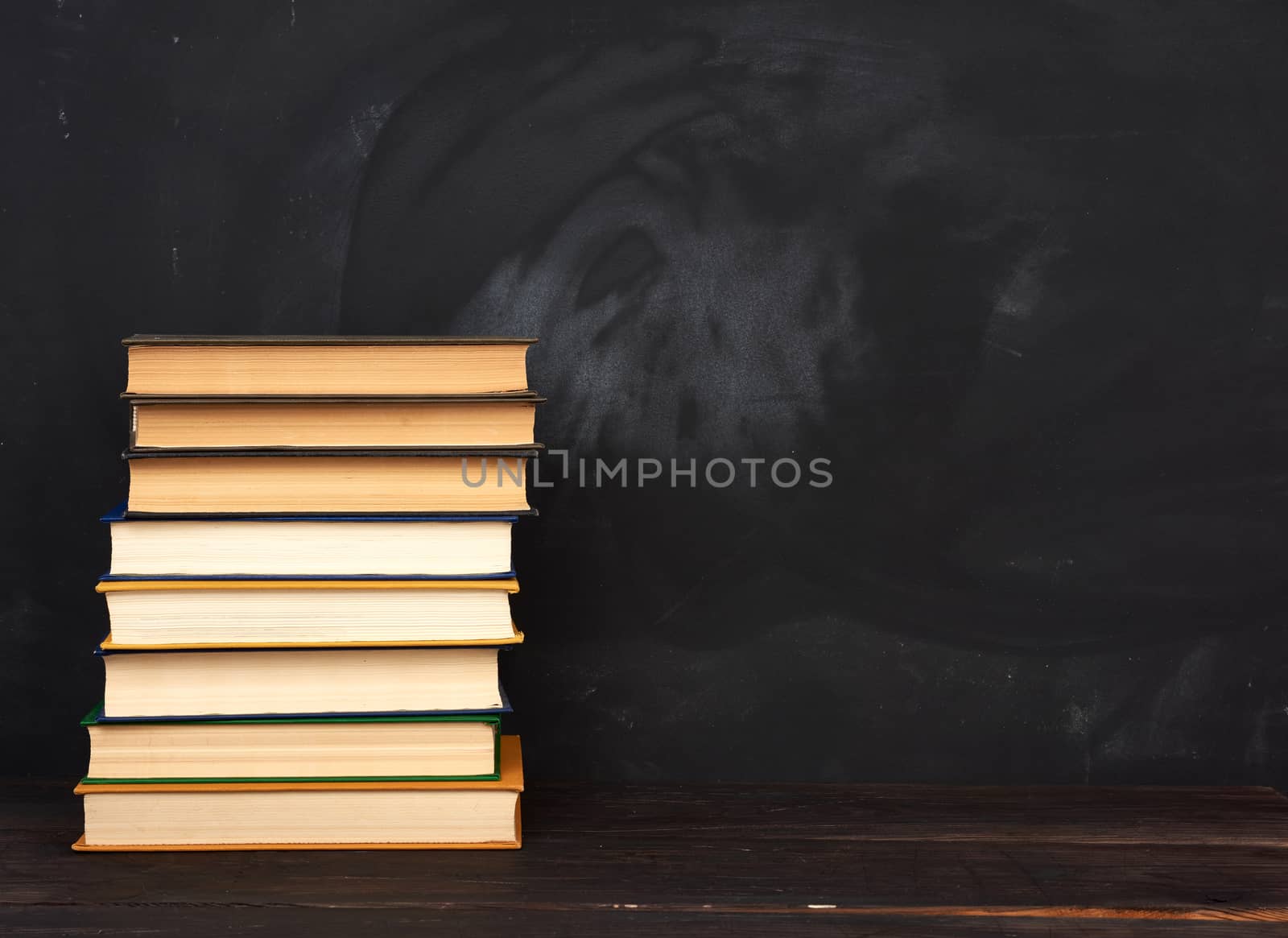 stack of various hardback books on the background of an empty black chalk board, place for text, back to school