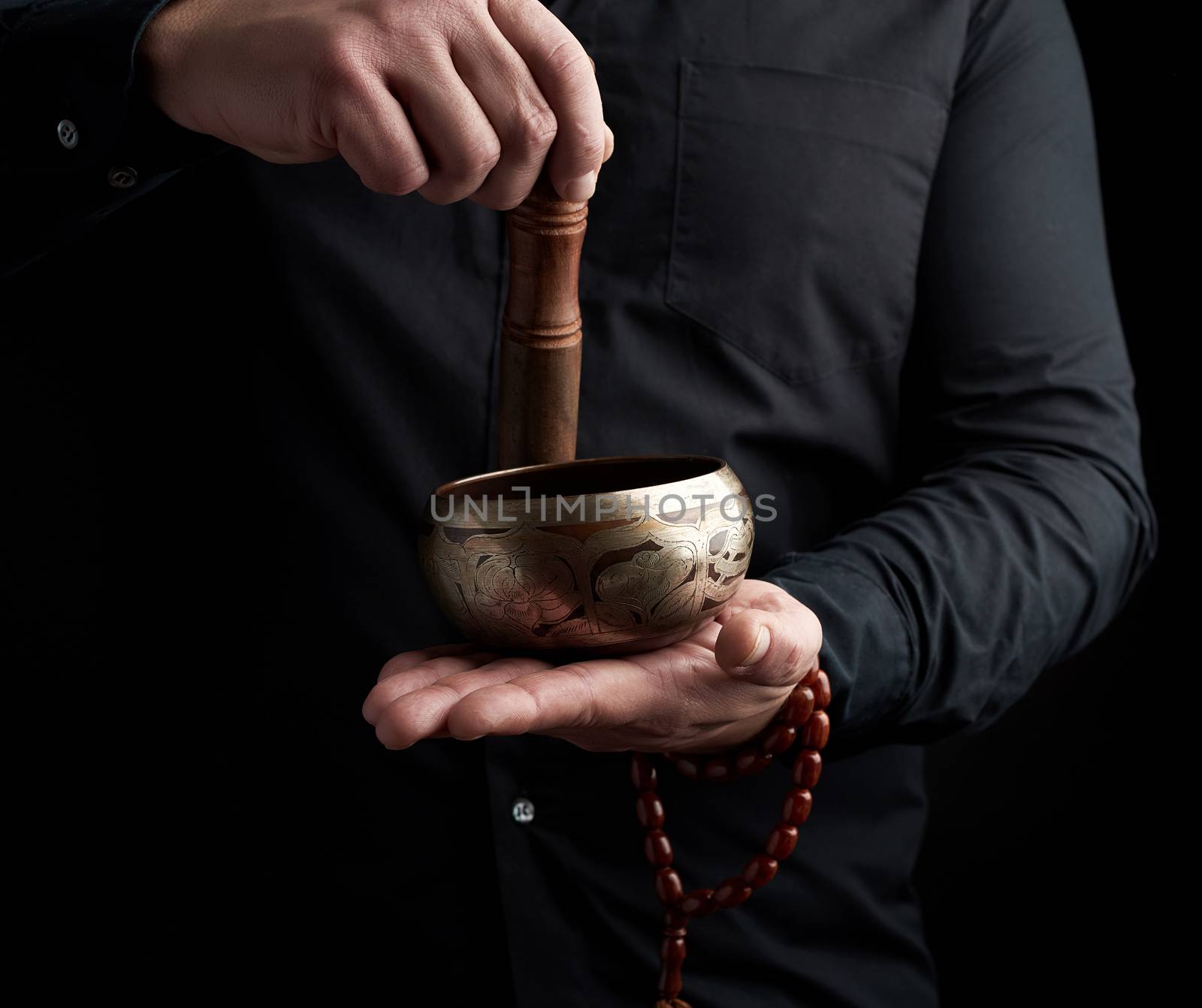 adult man in a black shirt rotates a wooden stick around a copper Tibetan bowl. ritual of meditation, prayers and immersion in a trance. Alternative treatment