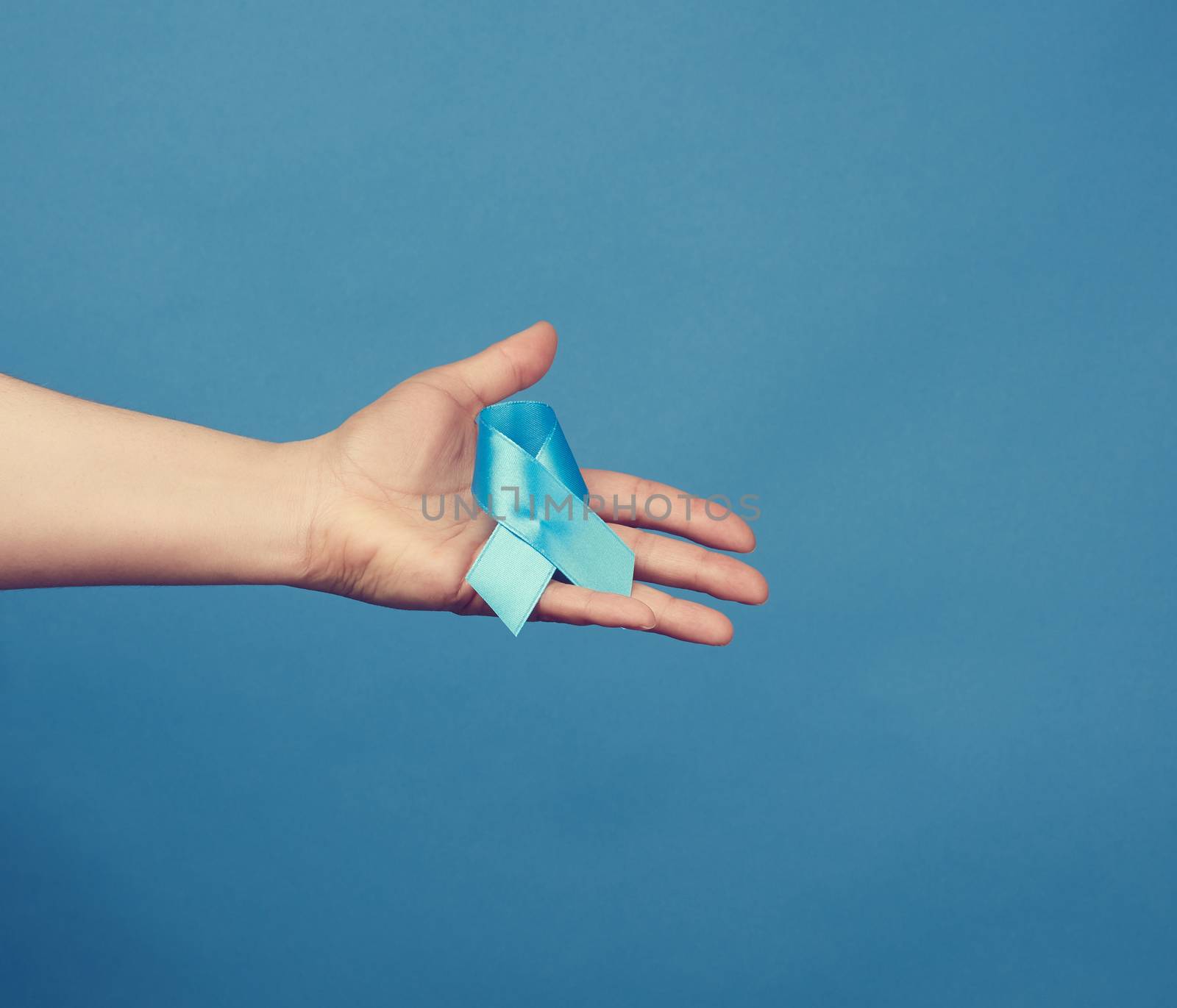 female hand holds blue silk ribbon in the shape of a loop on a blue background, symbol of the fight and treatment of prostate cancer