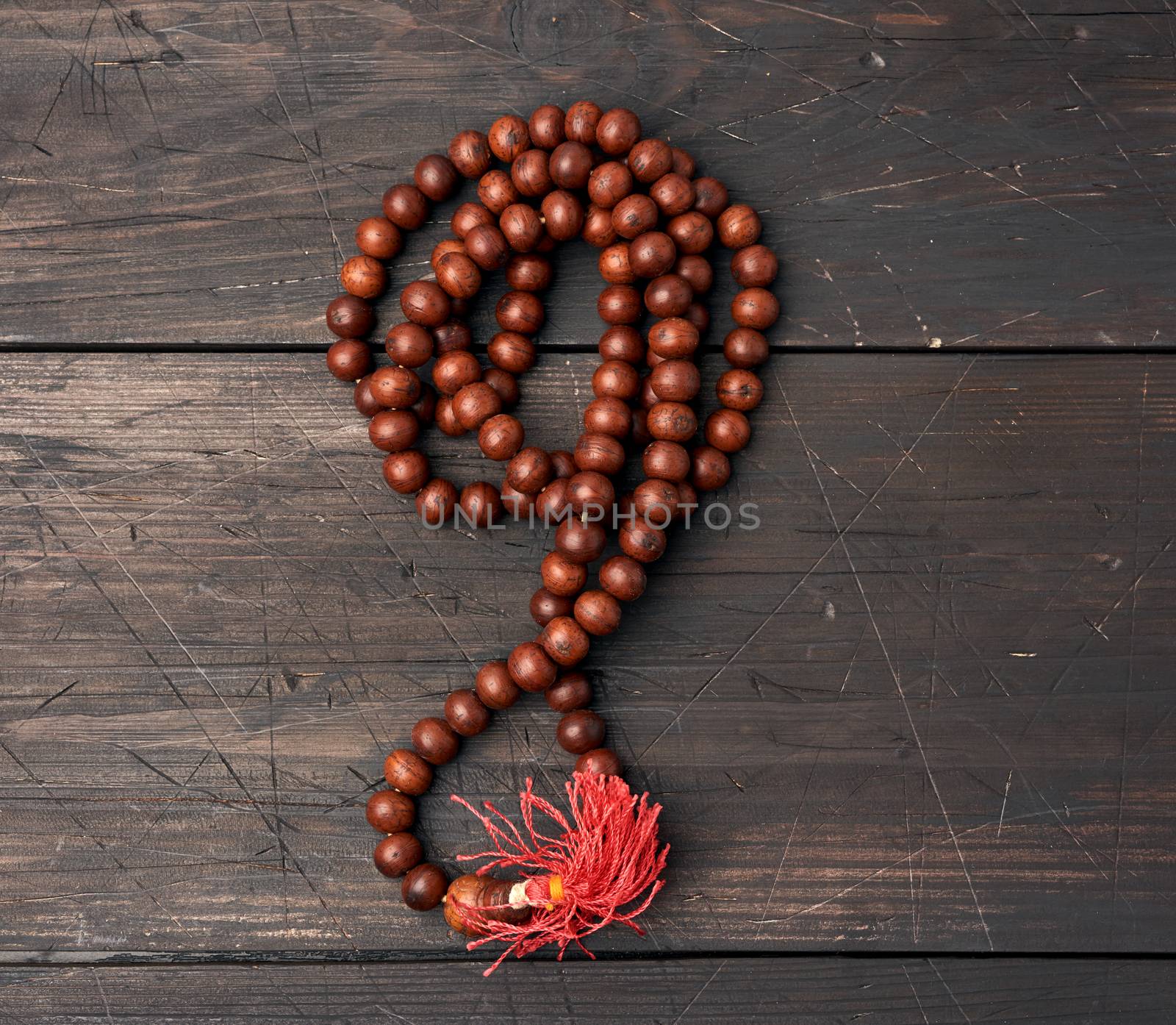 wooden prayer rosary on a brown wooden table, top view, close up