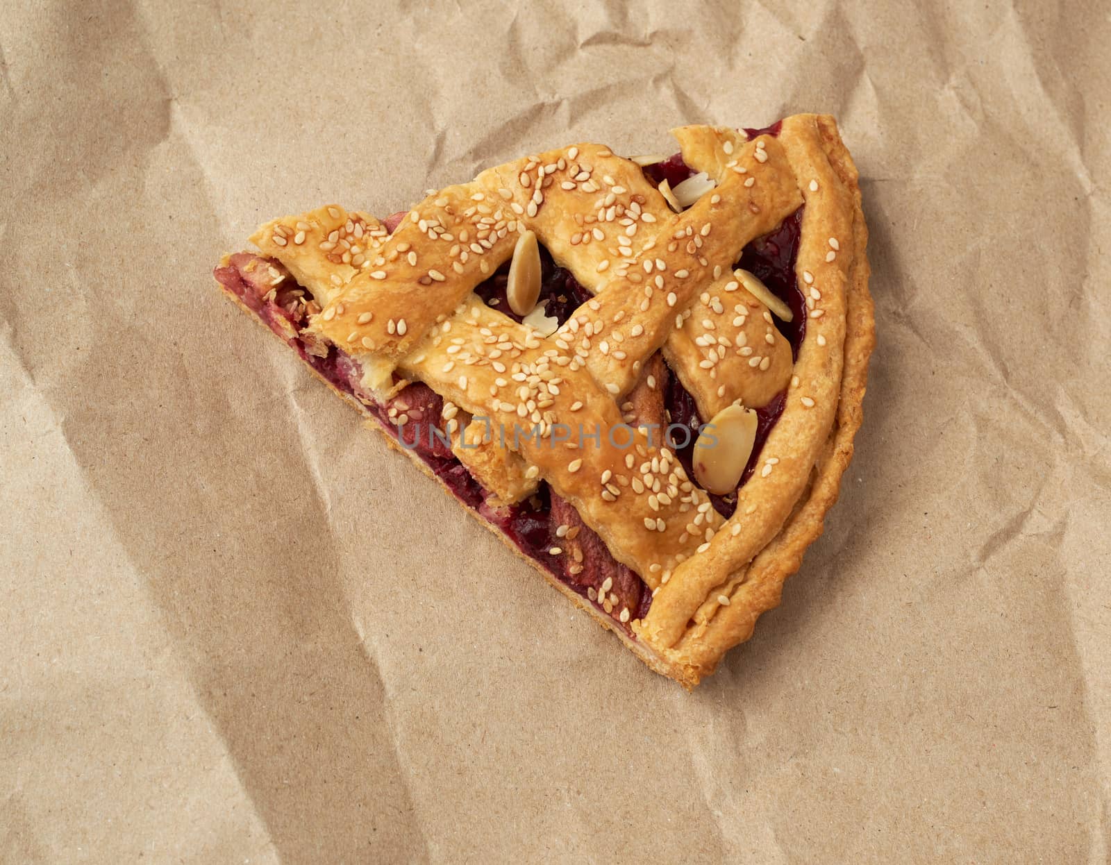 triangular slice of baked cherry pie on brown paper, top view, blue wooden background
