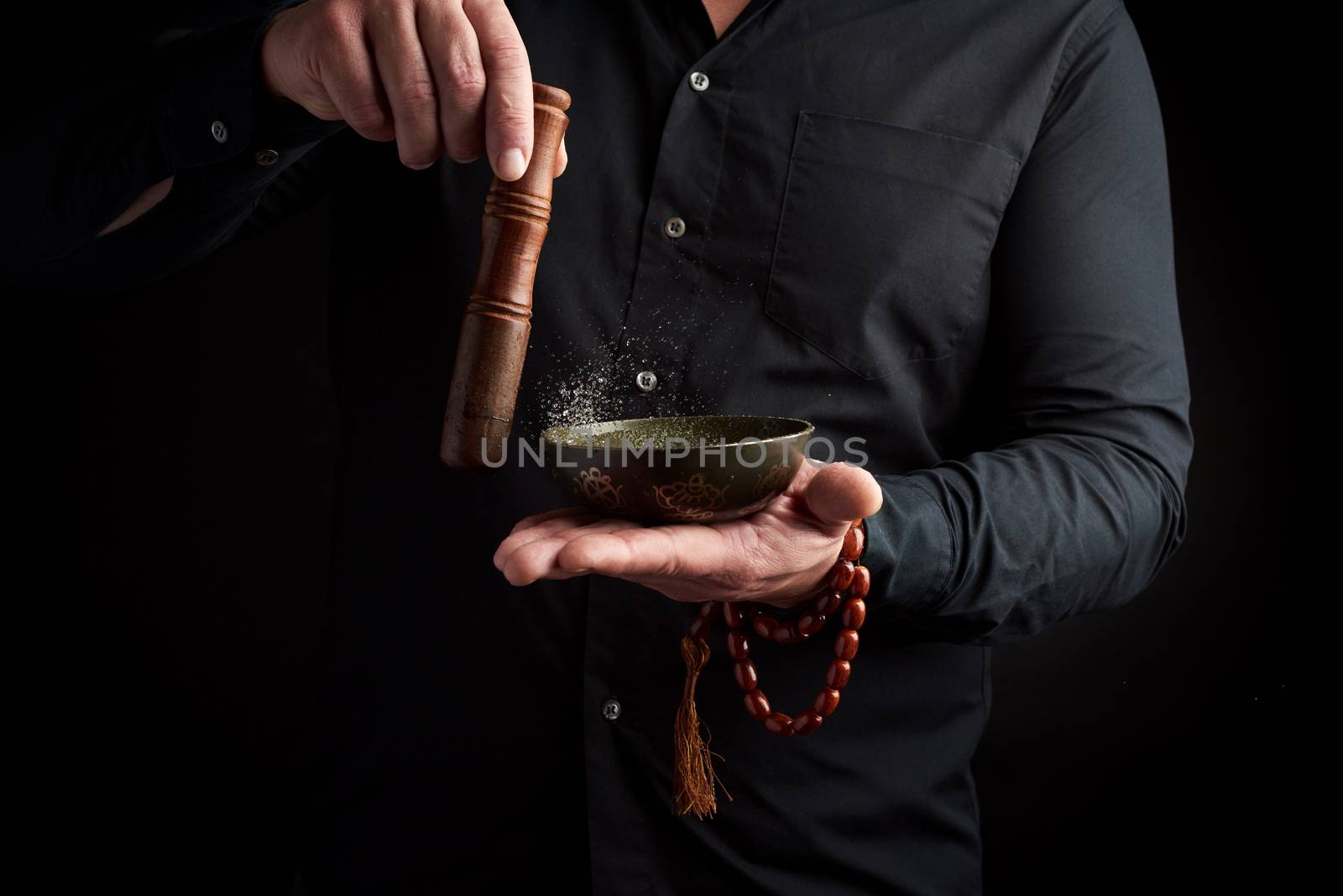 adult man in a black shirt rotates a wooden stick around a copper Tibetan bowl of water. ritual of meditation, prayers and immersion in a trance. Alternative treatment