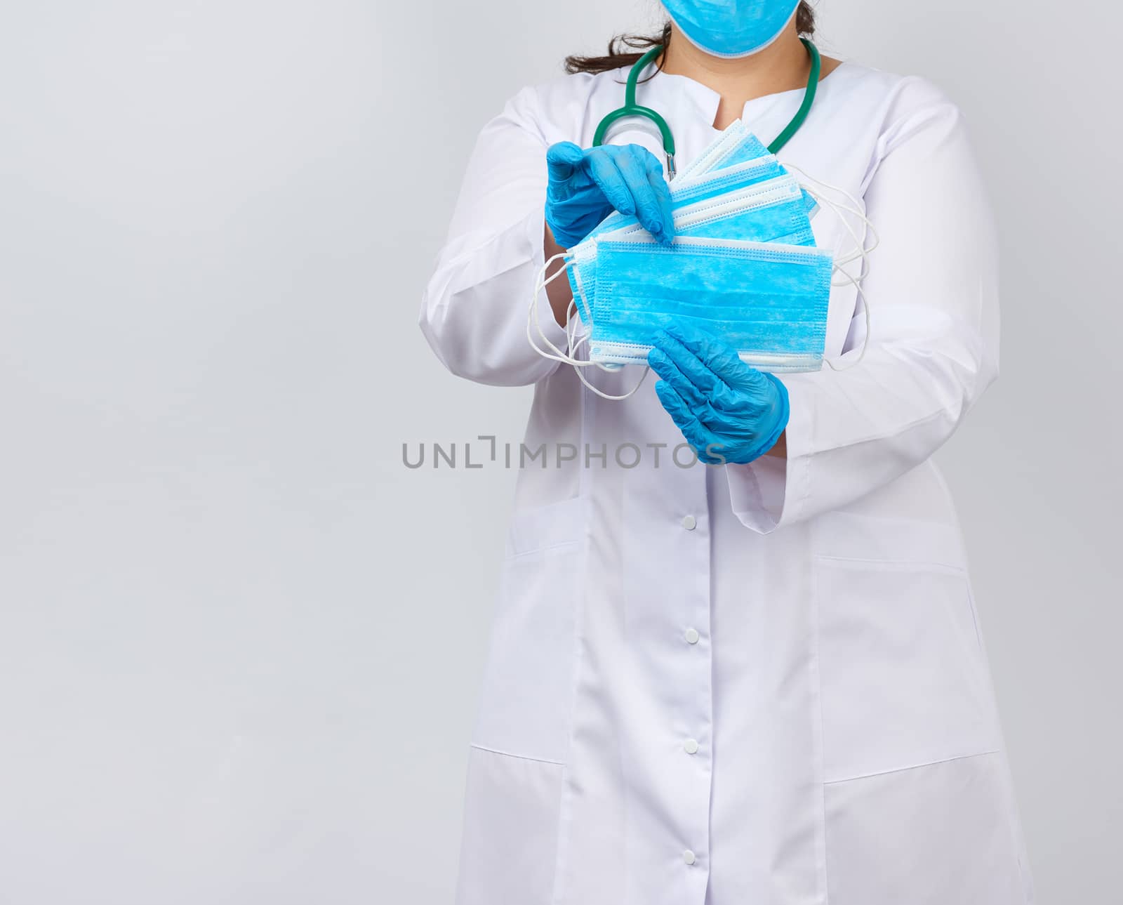 female doctor in a white coat and mask holds a stack of protecti by ndanko