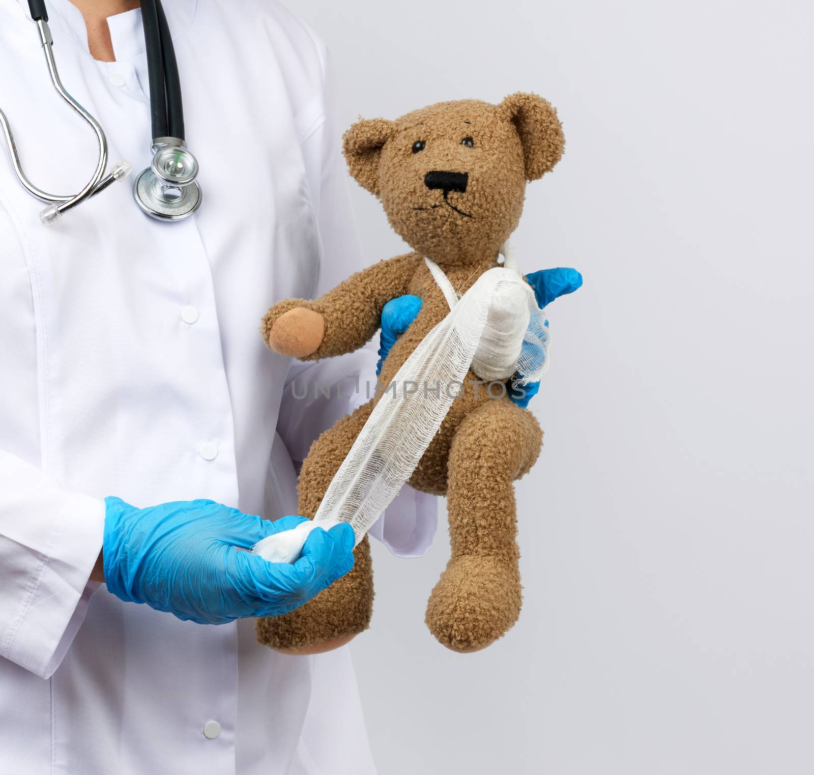 female medic holds brown teddy bear and bandages paw with white gauze bandage, concept of pediatrics and animal treatment