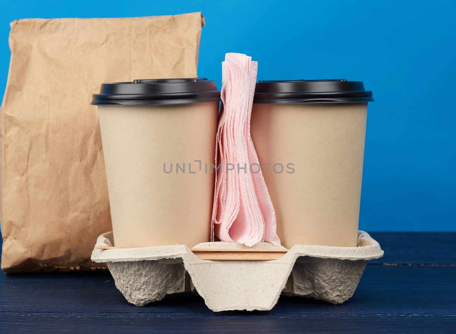 brown paper disposable cups with a plastic lid stand in the tray on a blue wooden table, takeaway containers