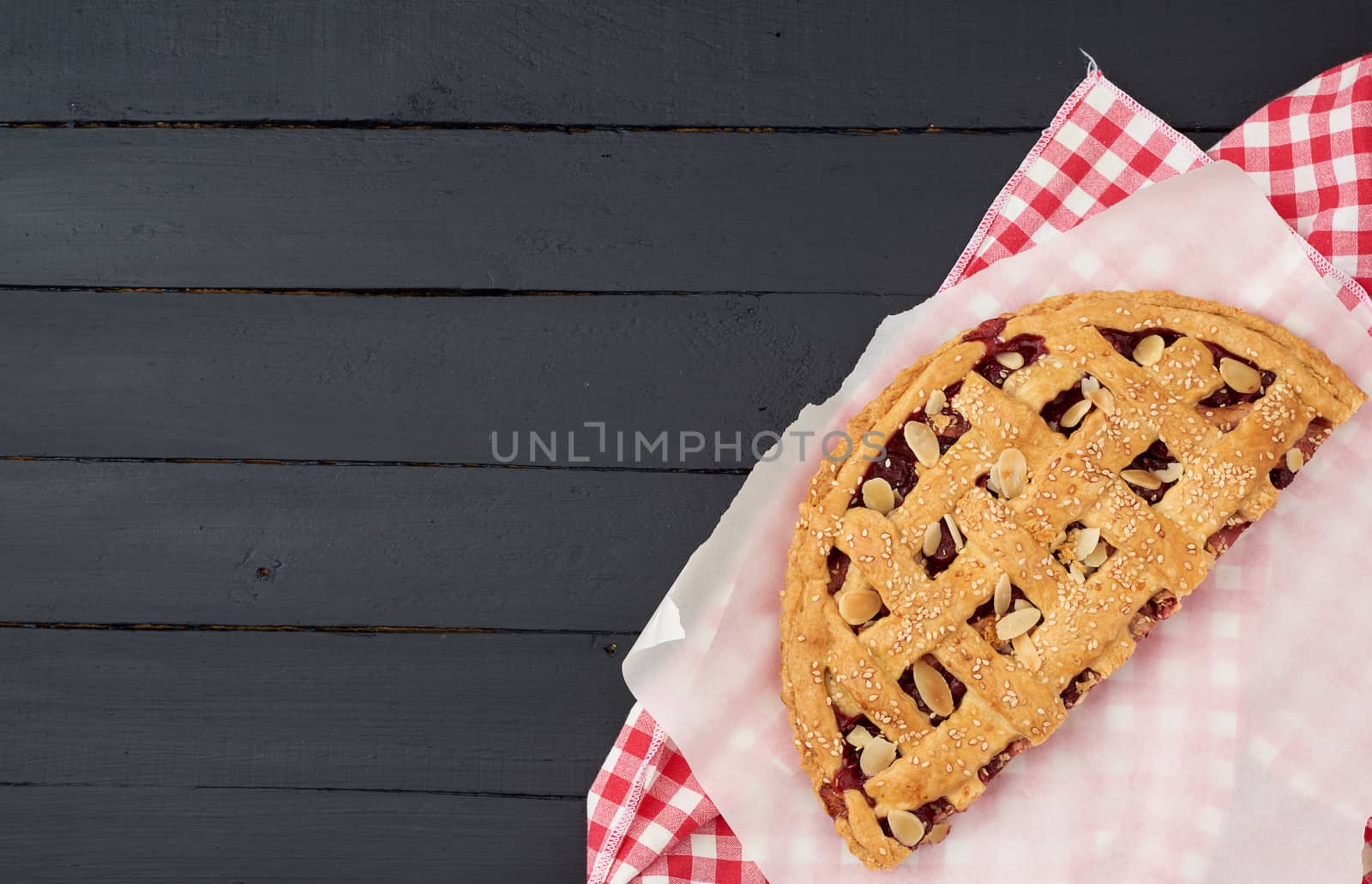 triangular slice of baked cherry pie on a white paper, top view, blue wooden background