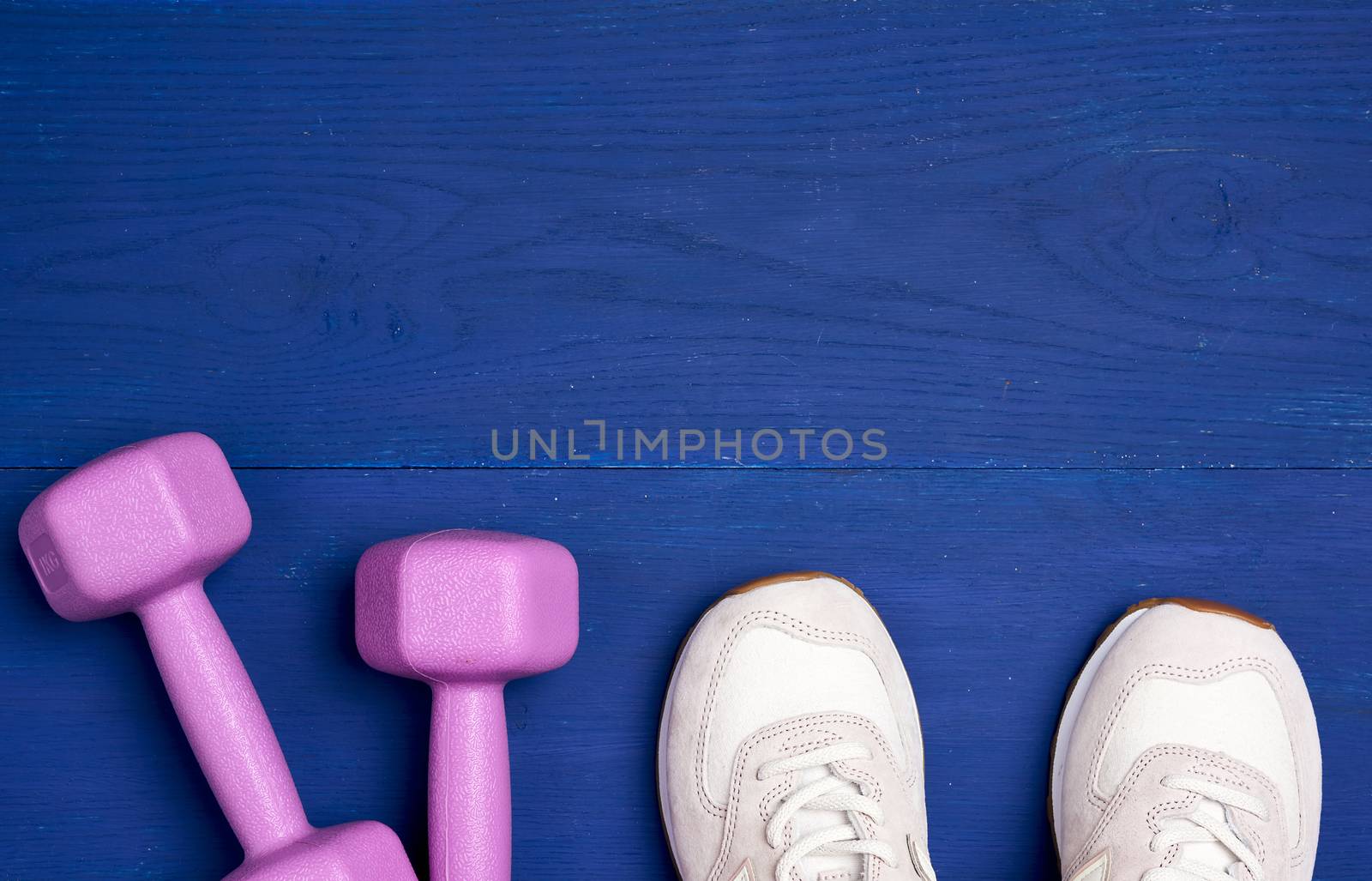pink plastic dumbbells of one kilogram and white sport shoe on a blue background, sports equipment, top view