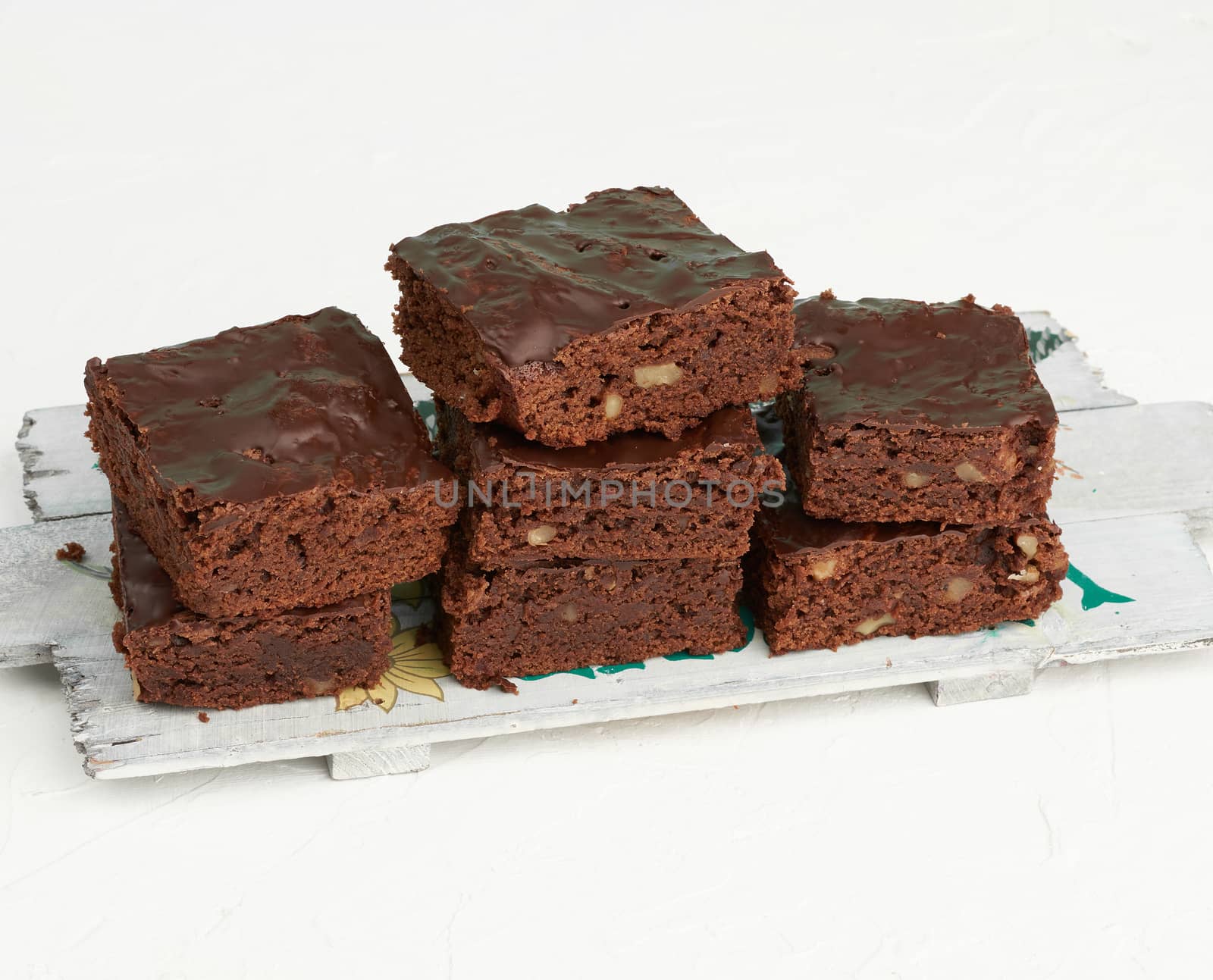 stack of square baked slices of brownie chocolate cake with walnuts on a wooden board, top view