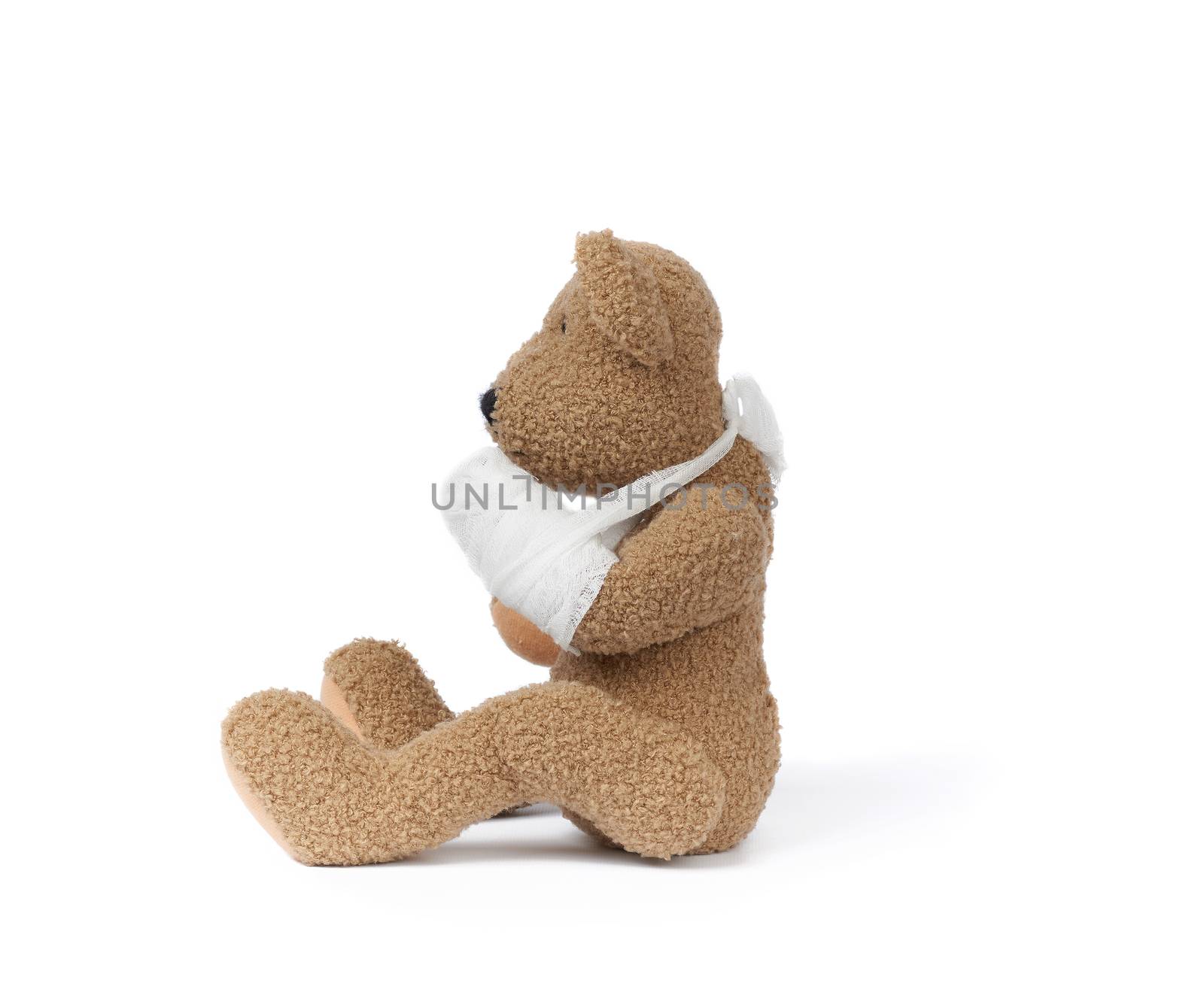 funny vintage brown curly teddy bear with rewound paw with white gauze bandage isolated on white background, concept of injuries in children or animals