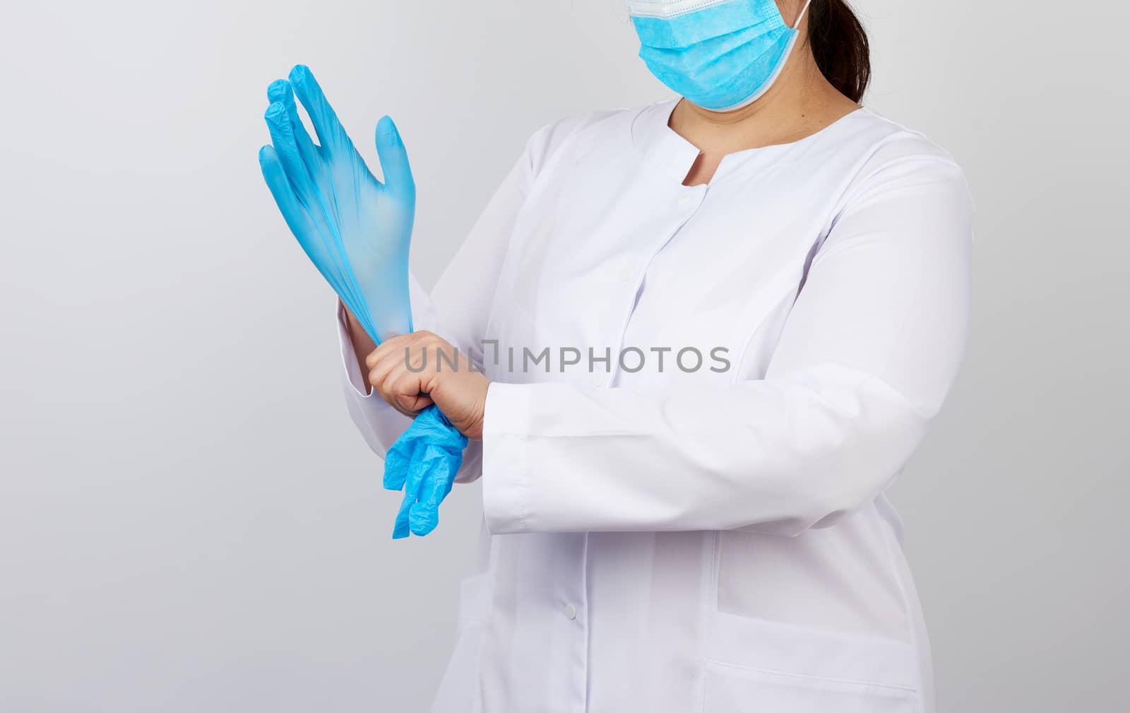 medical doctor in a white coat and mask puts on medical hands latex gloves before procedures, white studio background, copy space