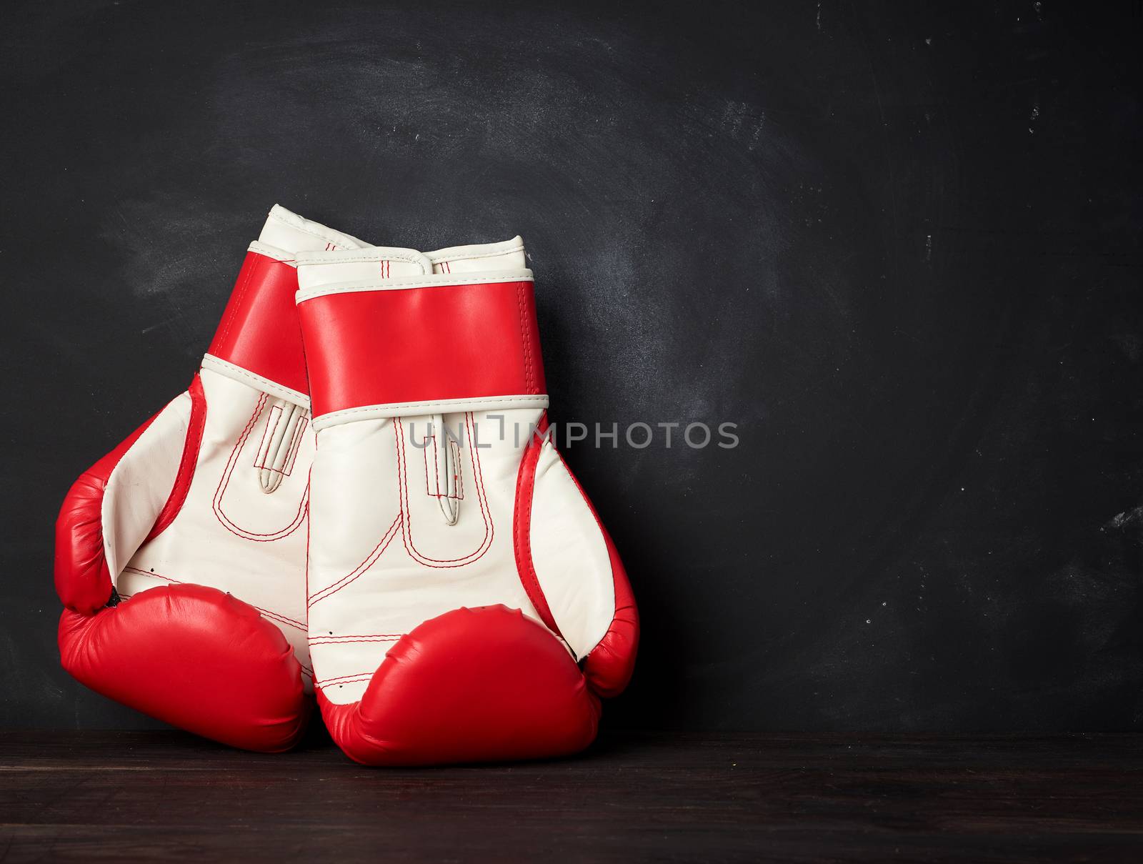pair of red-white leather boxing gloves on a black background, sports equipment, place for an inscription