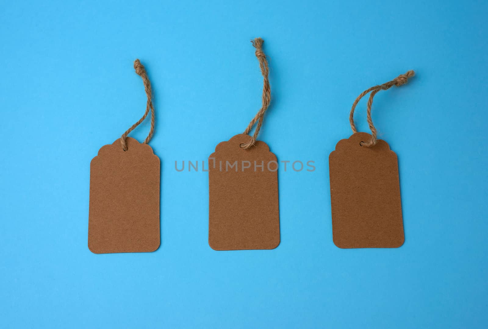 Empty brown paper tags tied with white string. Price tag, gift tag, sale tag  on the blue background, close up
