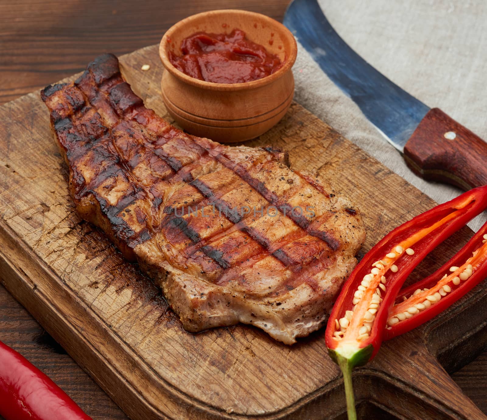 pork fried steak on the rib lies on a vintage brown wooden board, next to fresh red chili peppers, top view