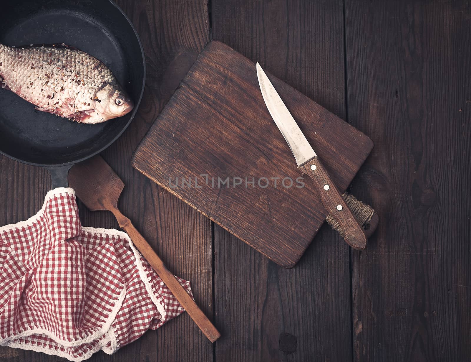 fresh crucian fish sprinkled with spices and lies in a black round pan, brown wooden table from boards, top view, copy space