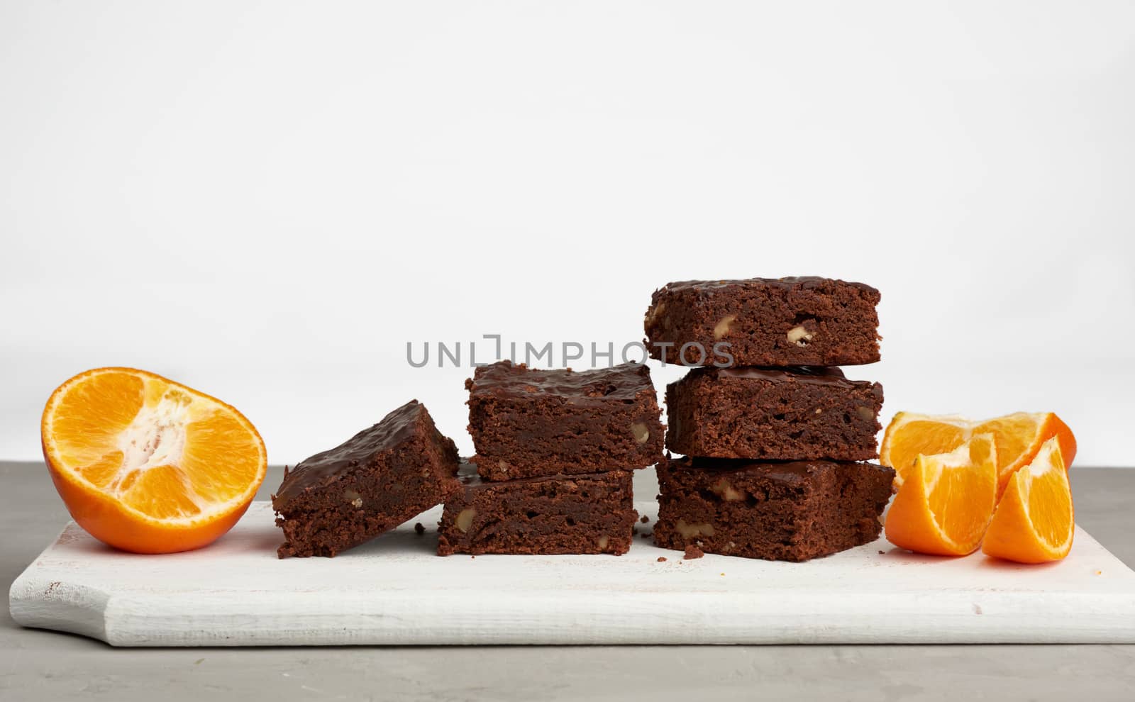 stack of square baked slices of brownie chocolate cake with walnuts on a white wooden board