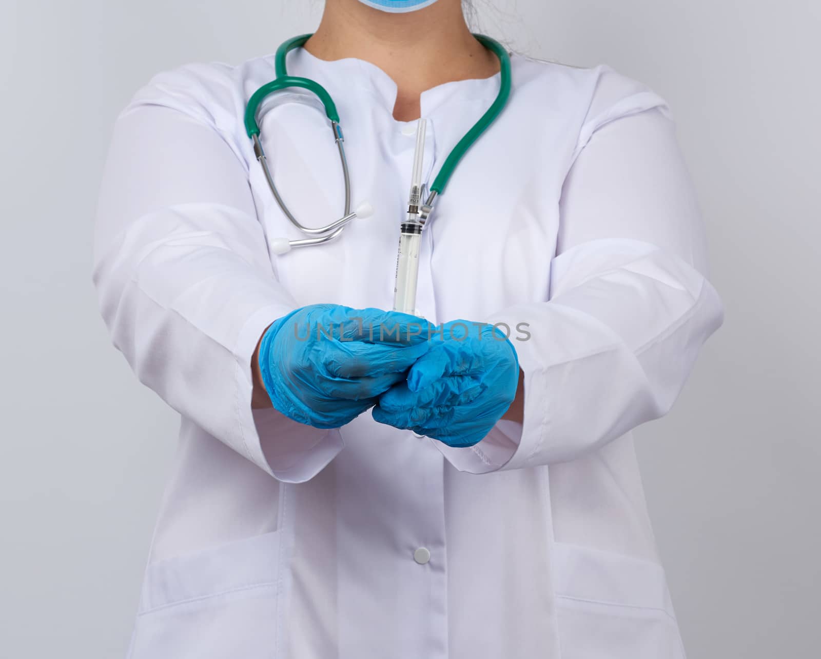 medic woman in white coat and blue latex gloves holding a syringe, white studio background, concept of timely vaccination against viruses
