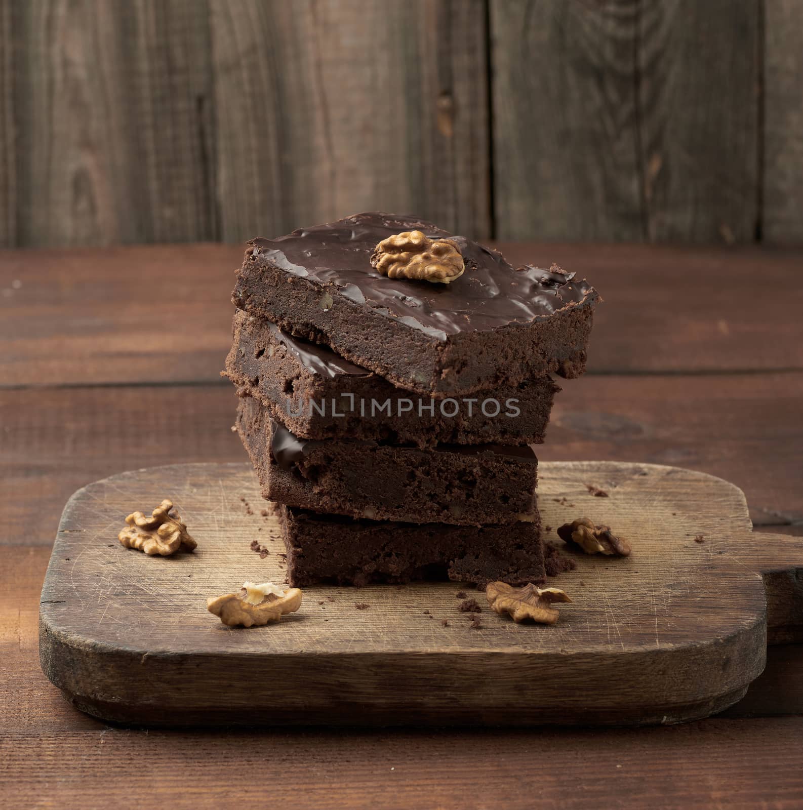 stack of square baked slices of brownie chocolate cake with walnuts on a wooden surface. Cooked homemade food. Chocolate pastry. Sweet meal, homemade dessert. Wooden table.