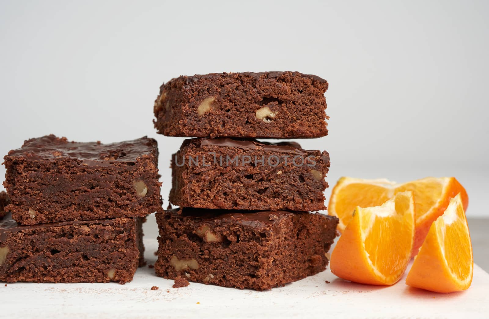 stack of square baked slices of brownie chocolate cake with walnuts on a white wooden board