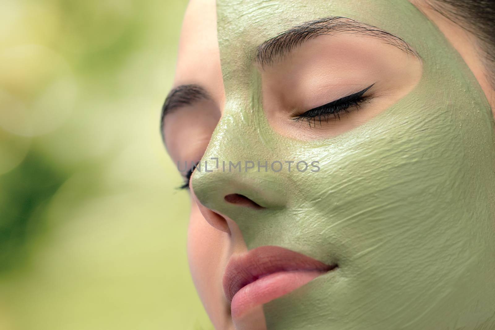 Macro close up head shot of attractive woman with green algae facial mask in spa.