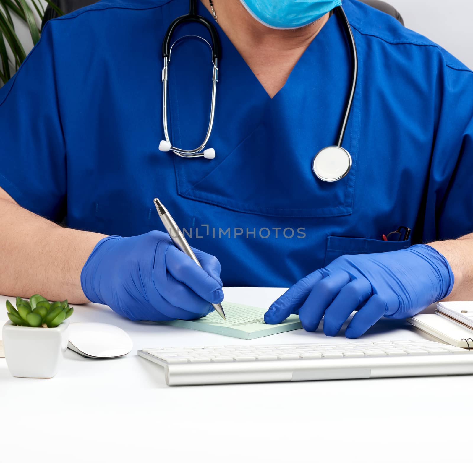doctor sitting at a white table in blue uniform and latex gloves, specialist writes a prescription for a pharmacy, medical office for receiving patients