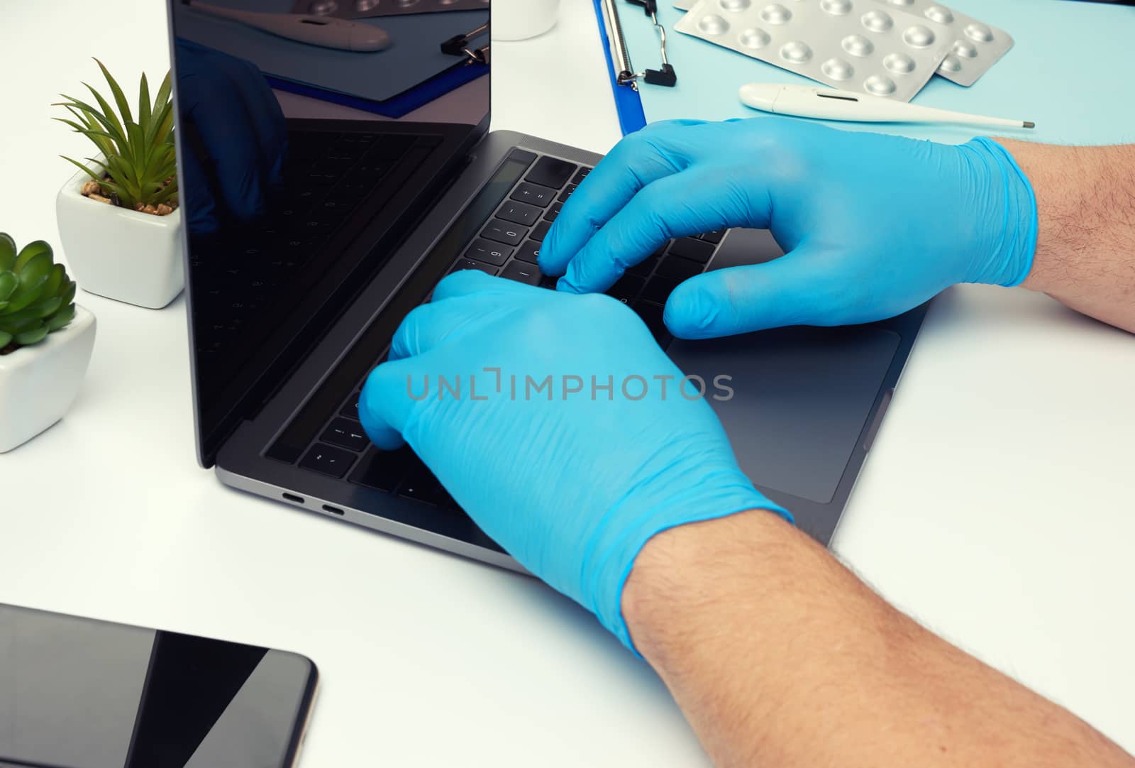 specialist doctor in blue latex medical gloves working on a laptop, concept of remote maintenance, therapist's workplace, top view