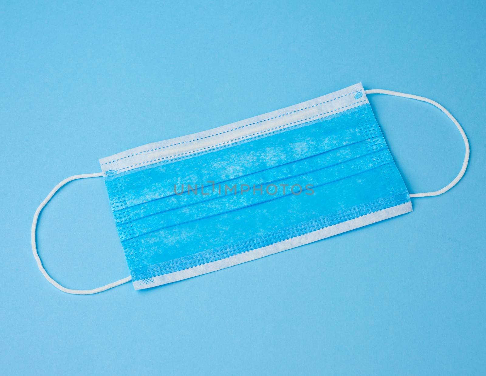 blue textile medical face mask with rubber bands from viruses and bacteria on a blue background, flat lay