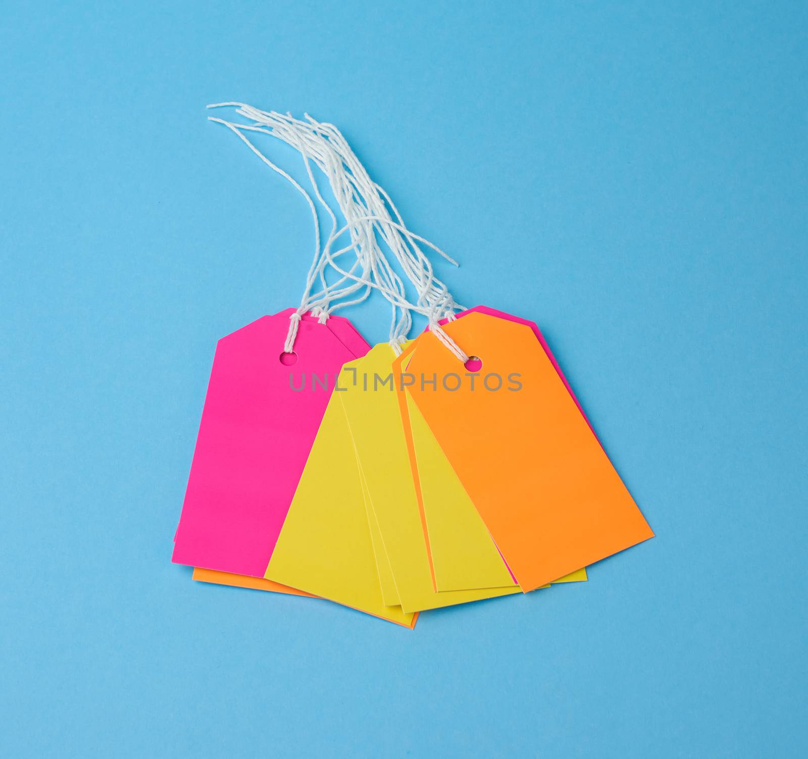 Stack empty color paper tags tied with white string. Price tag, gift tag, sale tag  on the blue background, close up