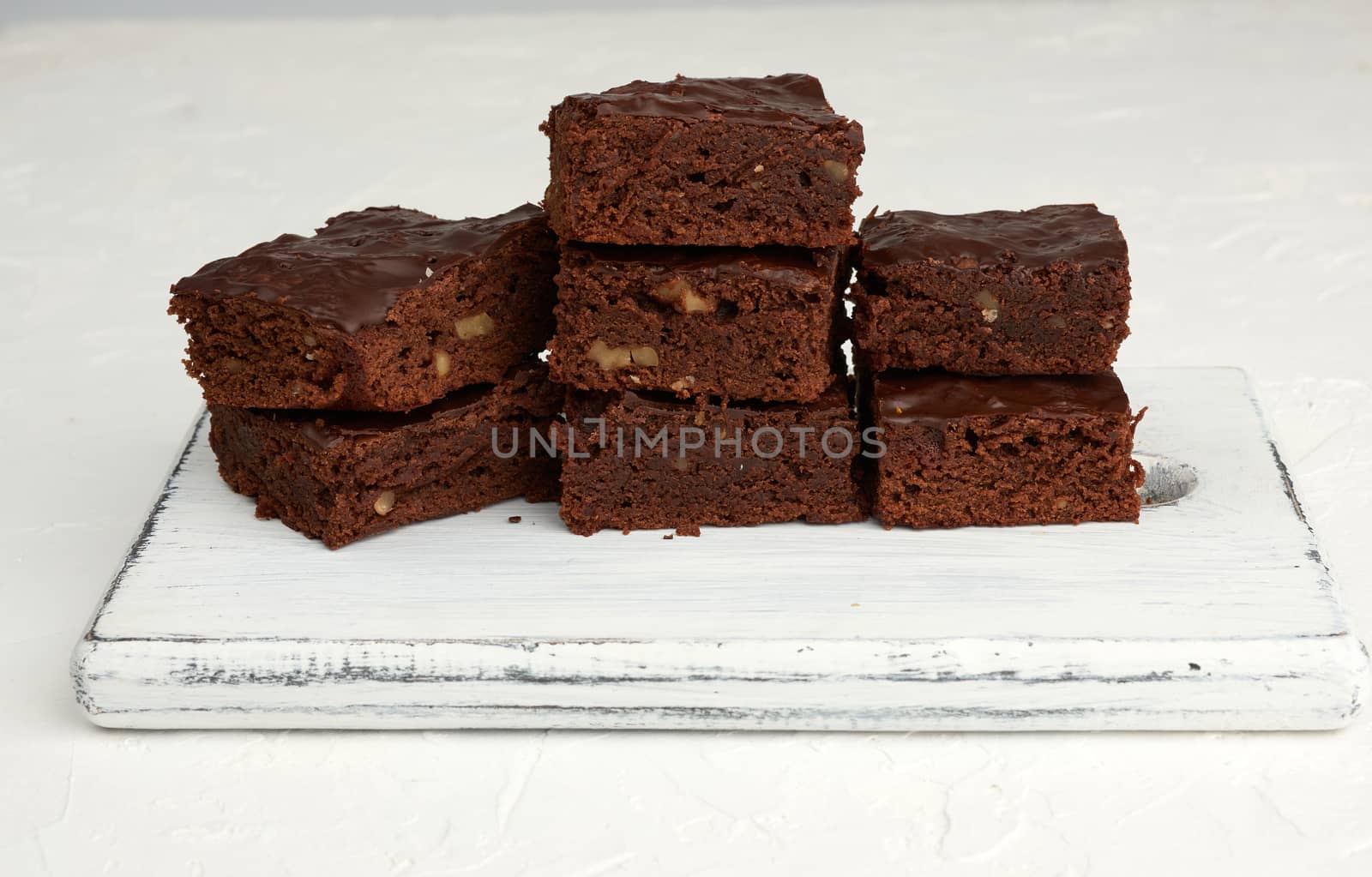 stack of square baked slices of brownie chocolate cake with walnuts on a white wooden board