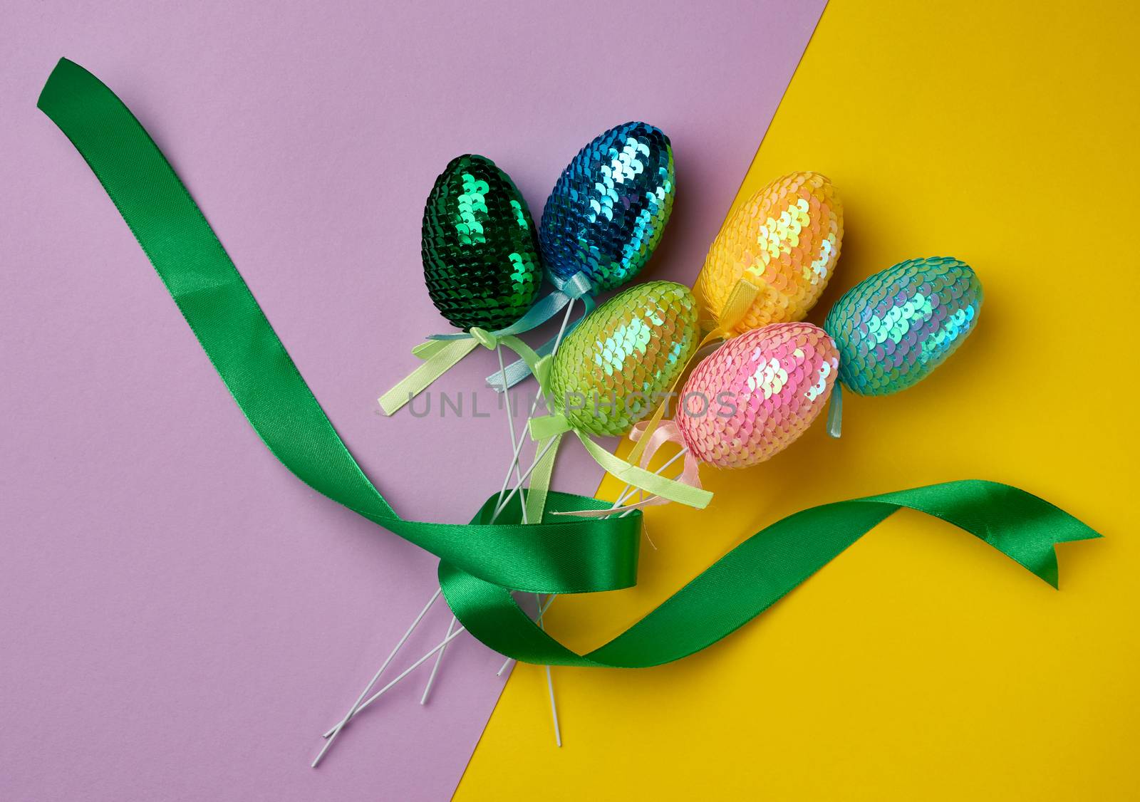 multicolored decorative Easter eggs decorated with sequins on a color background, festive backdrop, top view