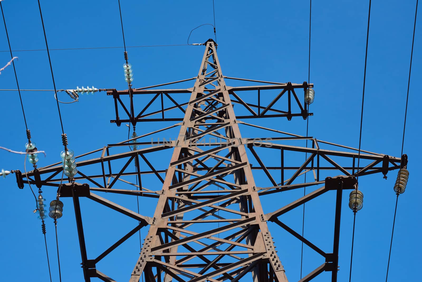 fragment of a metal tower with power lines against a blue sky