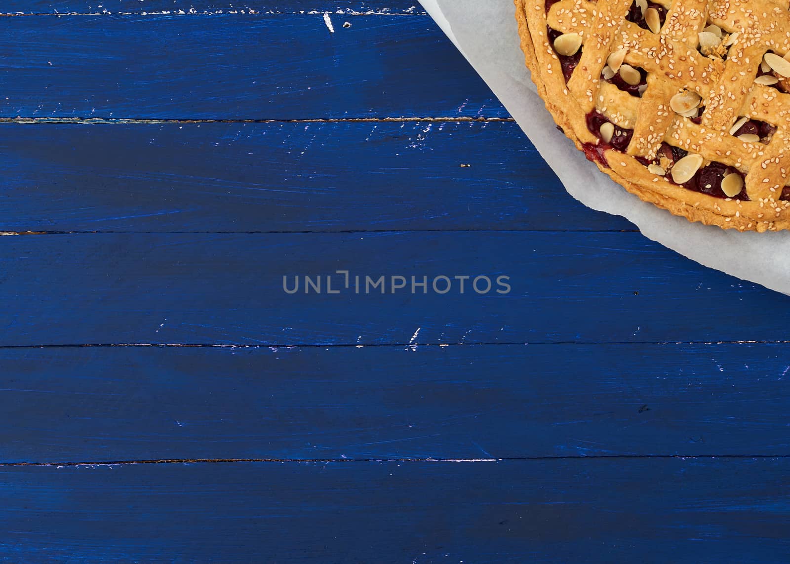 triangular slice of baked cherry pie on a white paper, blue wooden background 
