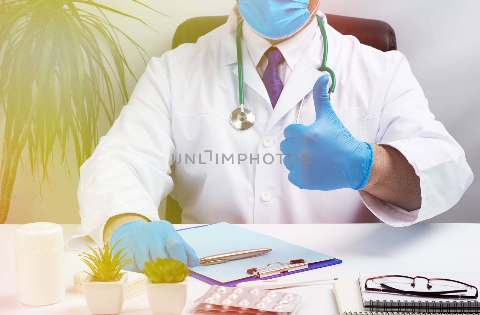male doctor in a white coat and blue latex gloves sits at a white desk in his office and shows gesture like, medical office