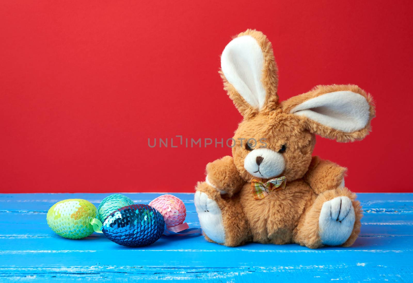 cute rabbit toy and decorative Easter eggs with sequins on a red background, festive backdrop