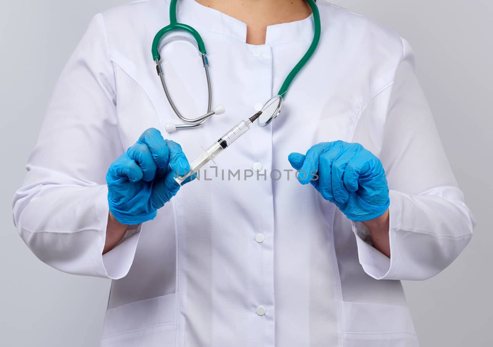 medic woman in white coat and blue latex gloves holds a syringe, white studio background, vaccination concept