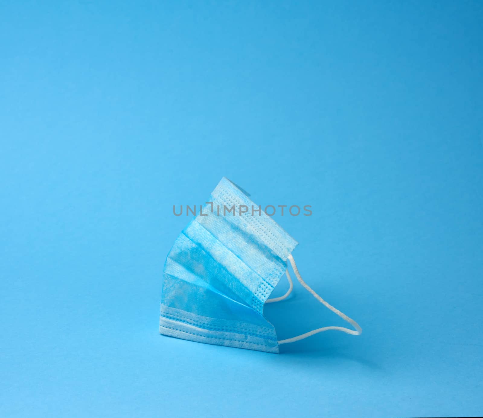 blue textile medical face mask with elastic bands folded, subject on blue background, element for designer