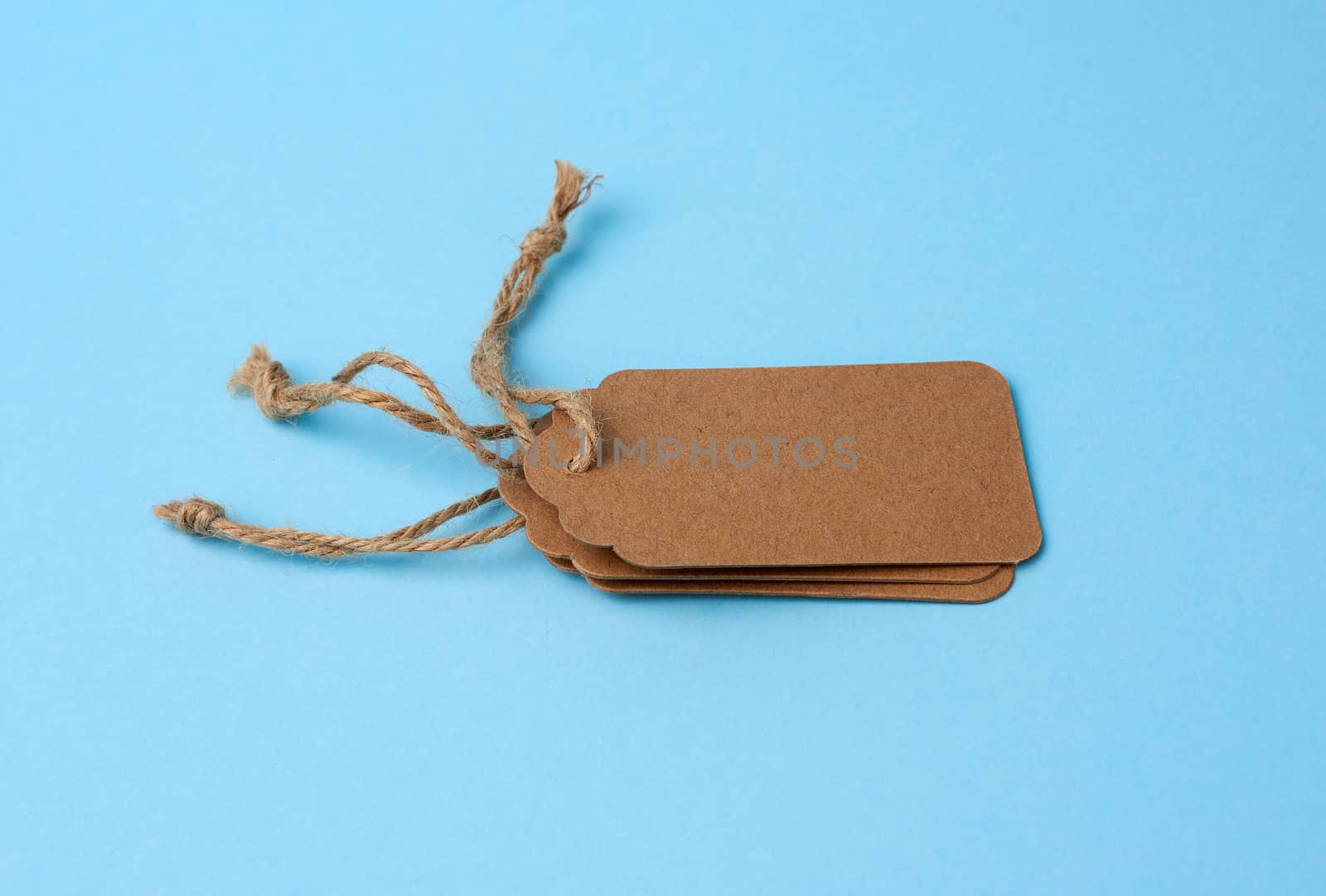 Empty brown paper tags tied with white string. Price tag, gift tag, sale tag  on the blue background, close up