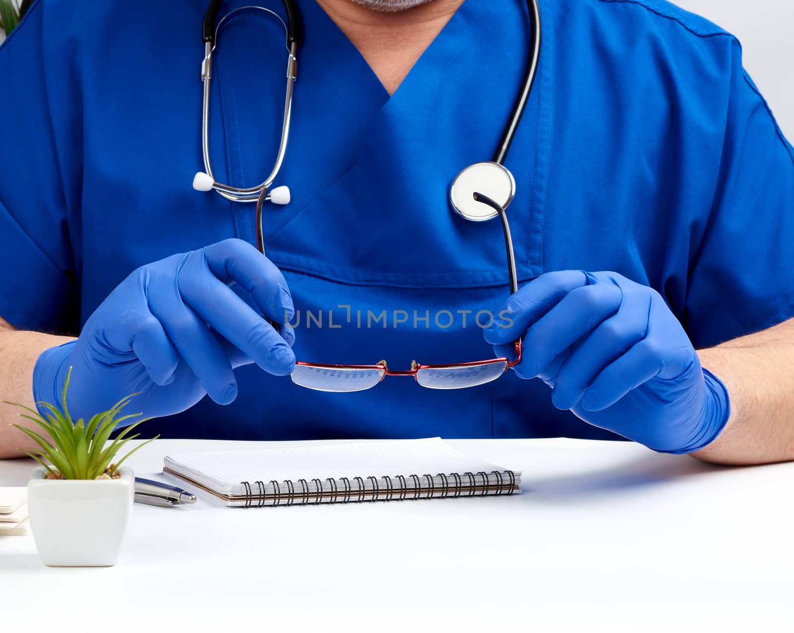 doctor in blue uniform and blue latex gloves sits at a white work table in his office, concept of patient reception in the clinic, therapist's workplace