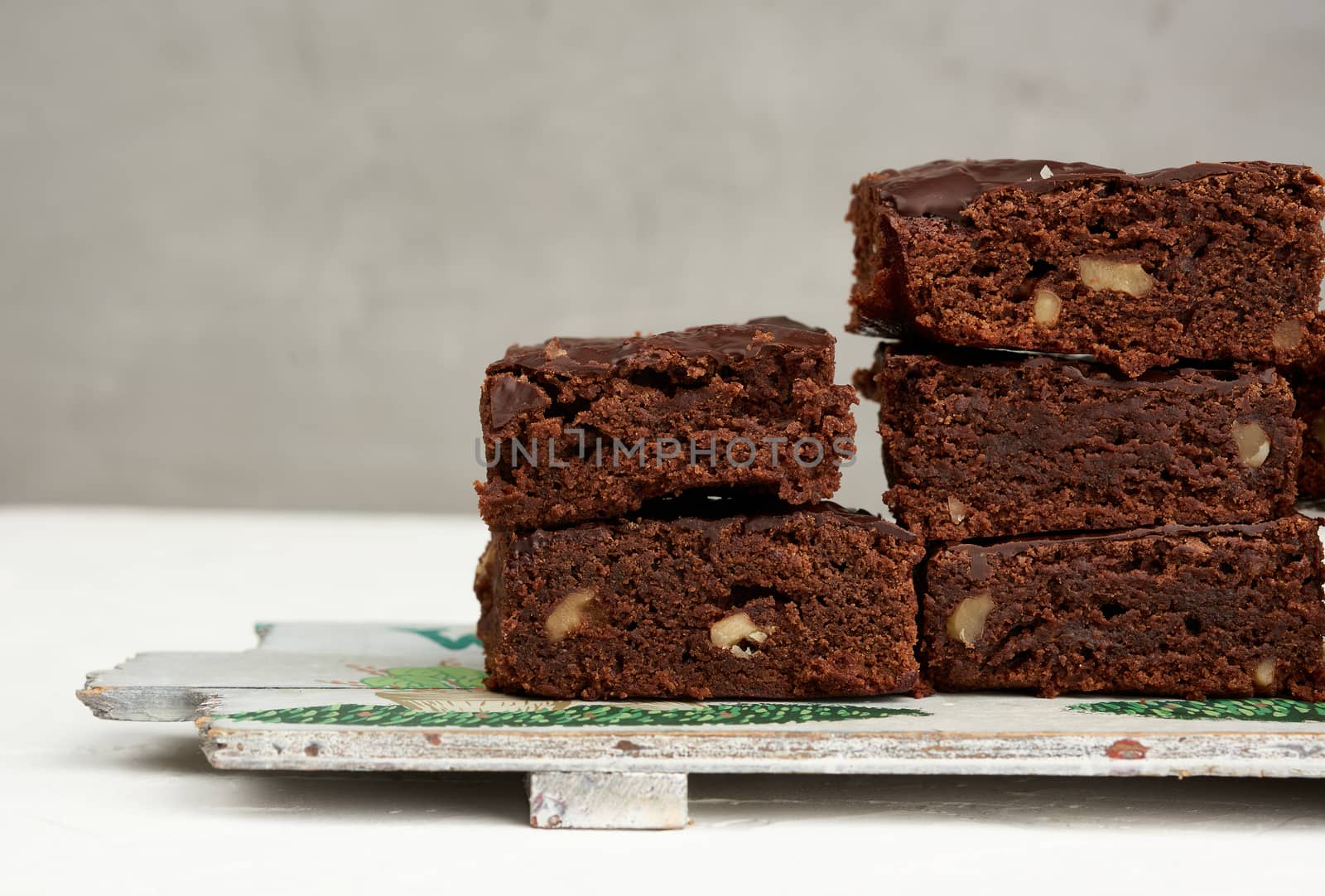 stack of square baked pieces of brownie chocolate cake with walnuts, on a wooden board, close up
