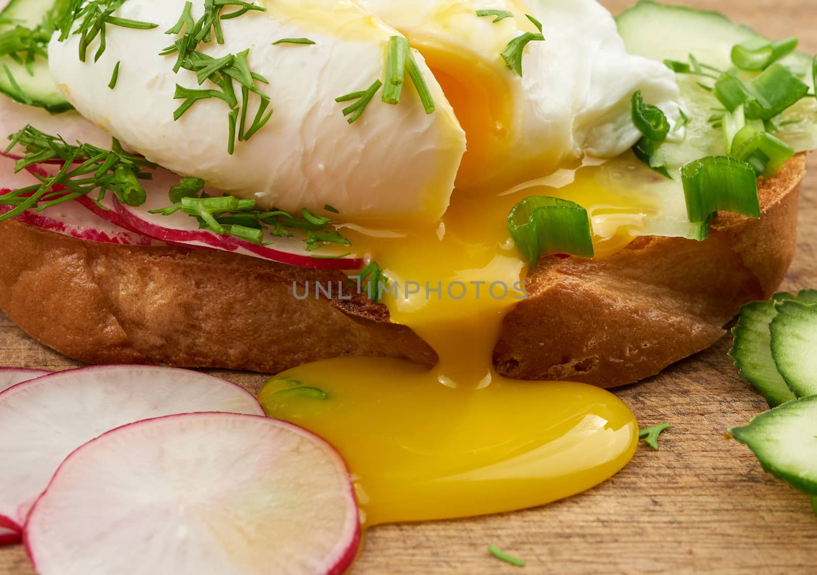 sandwich on toasted white slice of bread with poached eggs, dill and with slices of green onions, yellow yolk flows from the egg