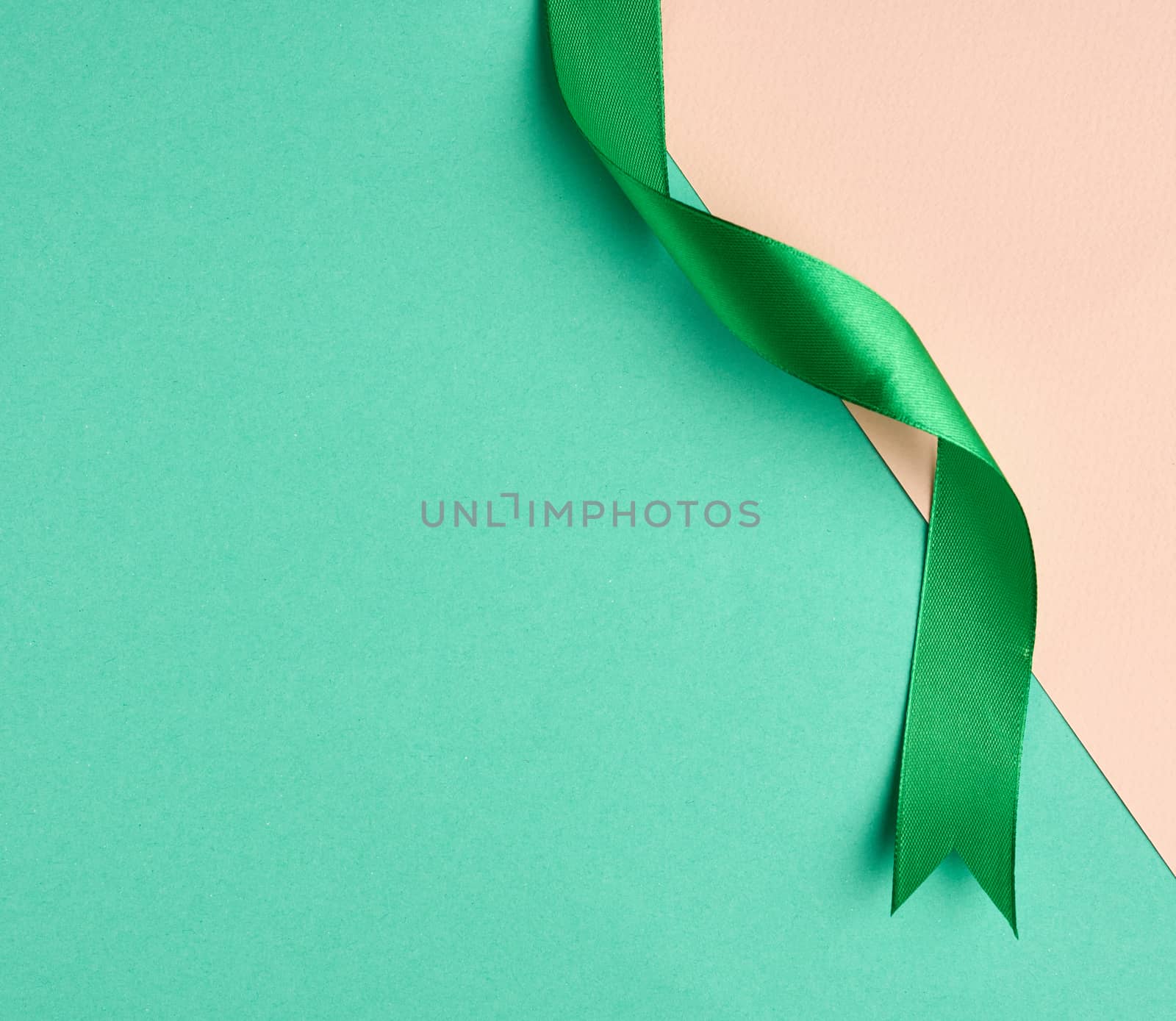 twisted silk green ribbon on a green-beige background, top view, cropped end