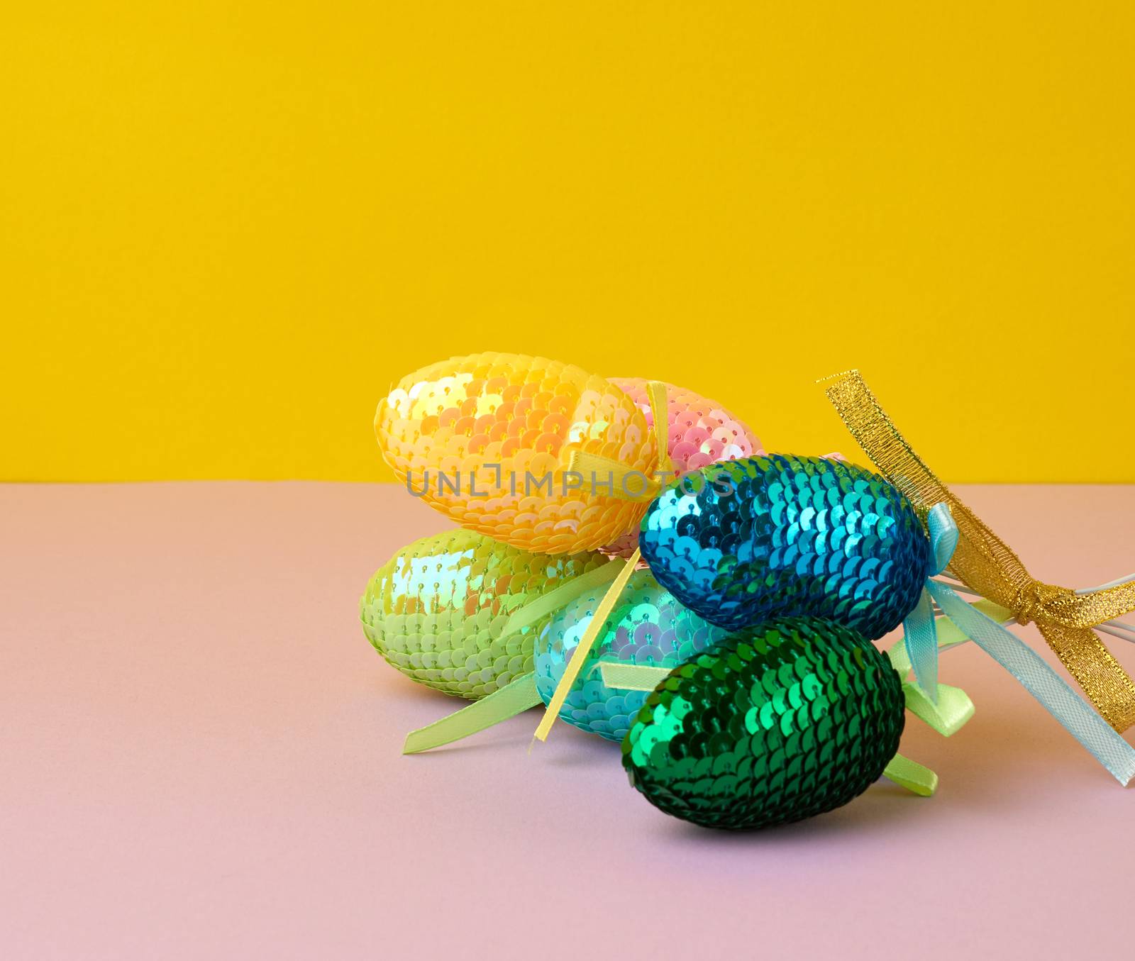 multicolored decorative Easter eggs decorated with sequins on a color background, festive backdrop, top view