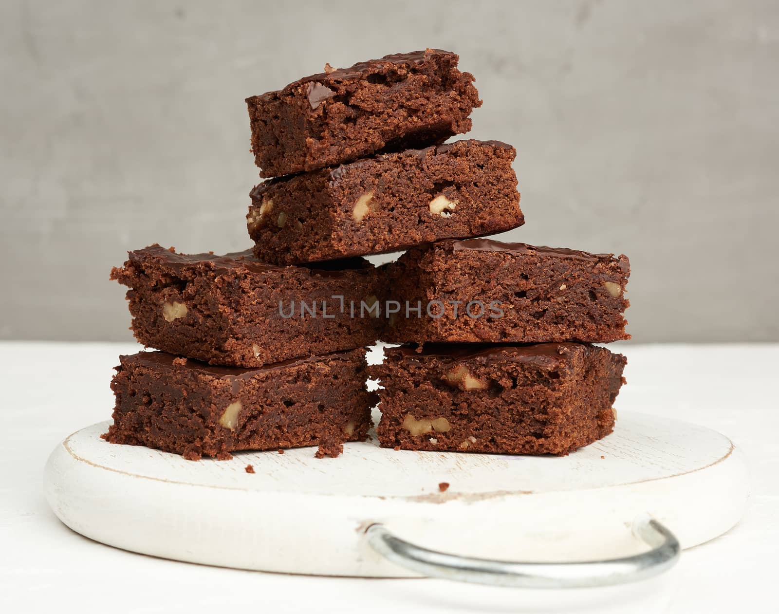 stack of square baked slices of brownie chocolate cake with walnuts on a round white wooden board