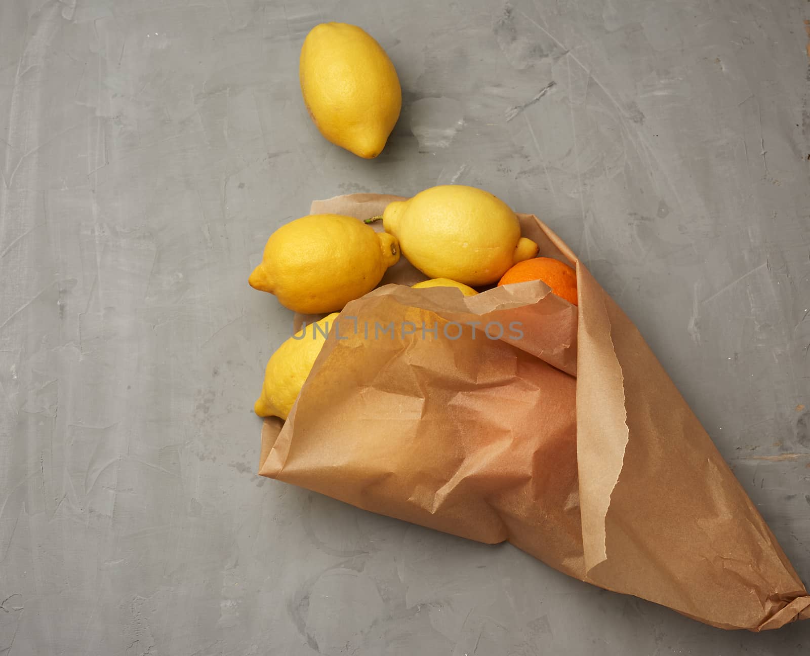 ripe yellow lemons in a brown paper bag on a gray background, top view