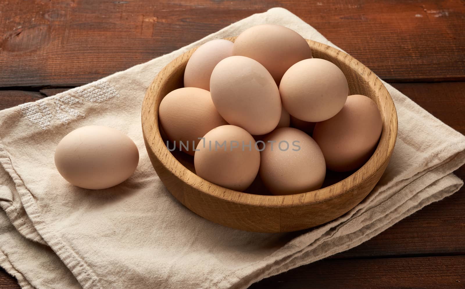 raw brown homemade chicken eggs in a wooden plate on the table, top view