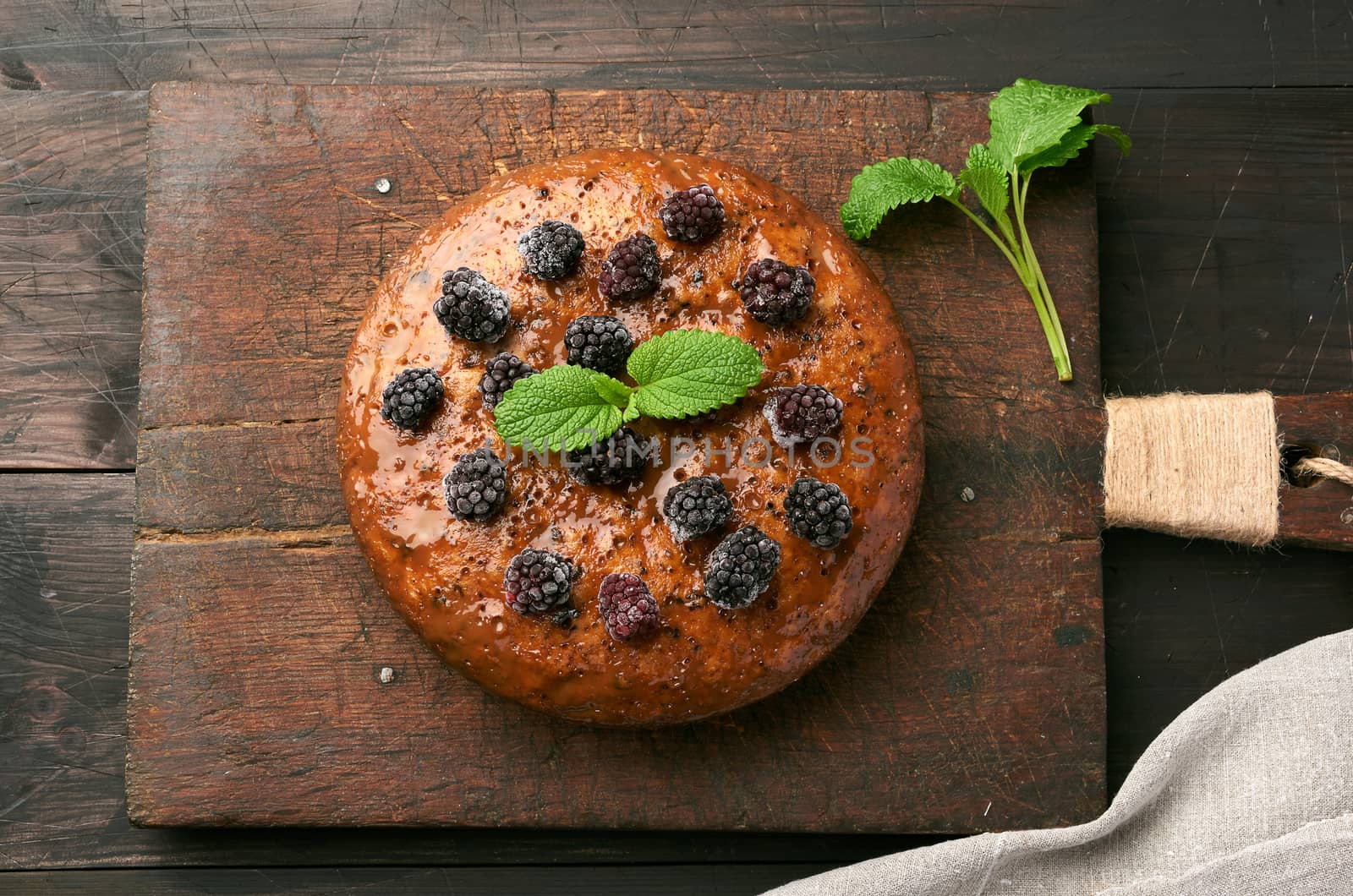 baked round biscuit cake with nuts and berries topped, wooden brown table, top view